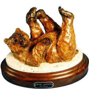 Bronze grizzly bear rolling playfully on its back on a round wood base