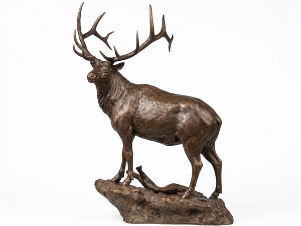 Bronze bull elk sculpture by Eric Thorsen with a full rack of antlers, standing on a rocky base beside a fallen branch