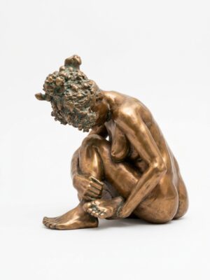 Bronze sculpture of a nude woman seated with her knees drawn up, leaning forward over her feet with her hair gathered on top of her head, in a golden bronze patina