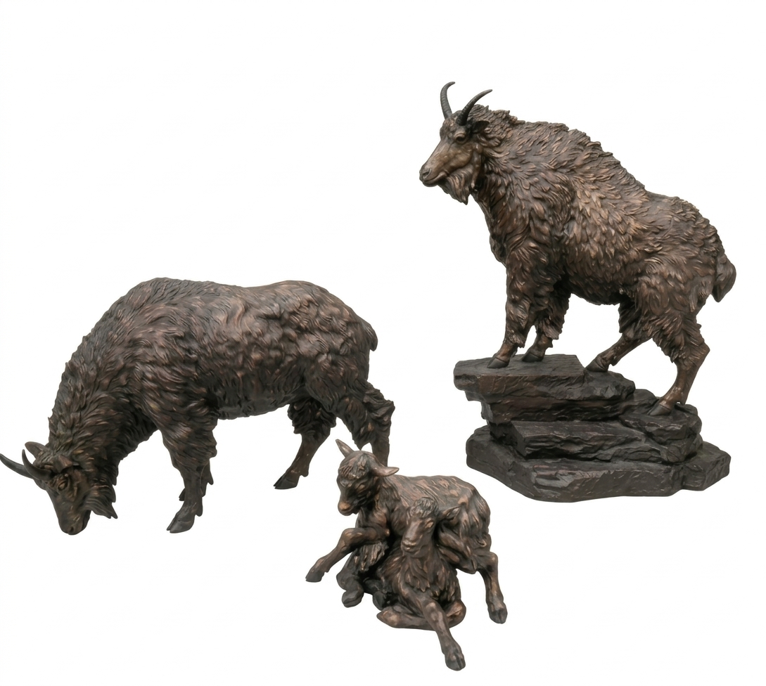 Bronze sculpture group of a mountain goat family: an adult goat standing on a rocky base, a second adult grazing and a kid lying down, on a white background